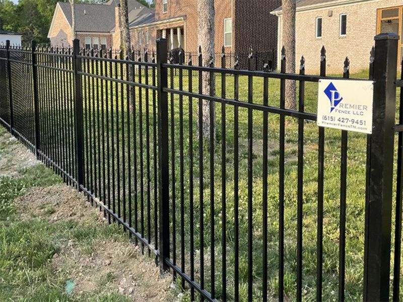 A black metal fence surrounds a lush green yard in front of a house.