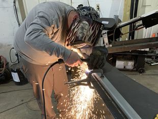A man wearing a welding helmet is welding a piece of metal.