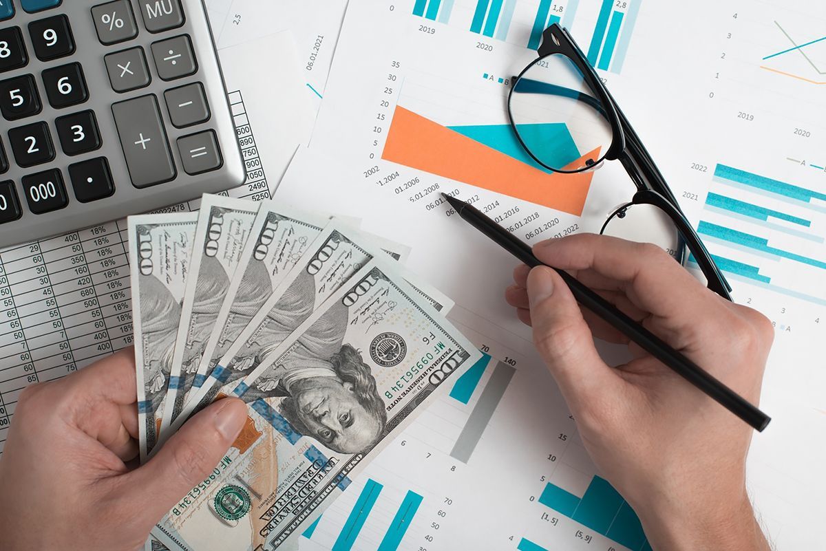 A person is holding a bunch of money and writing on a piece of paper.