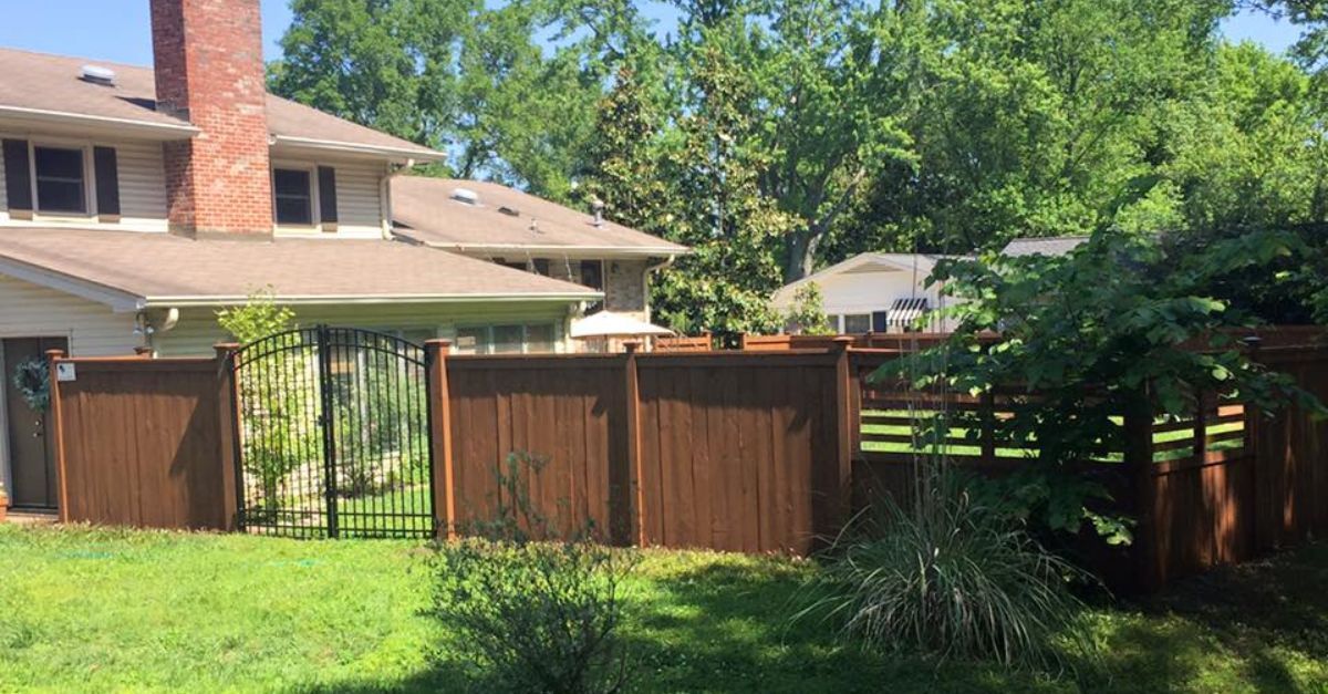 Brown wooden fence surrounding a grassy backyard with a house visible.