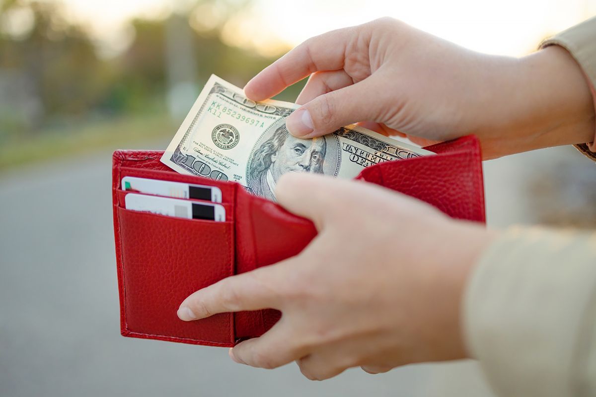A person is taking money out of a red wallet.