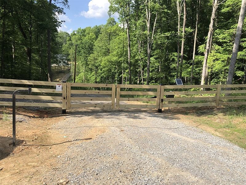 A wooden fence surrounds a gravel road in the woods.