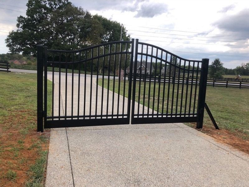 A black gate is open to a concrete driveway