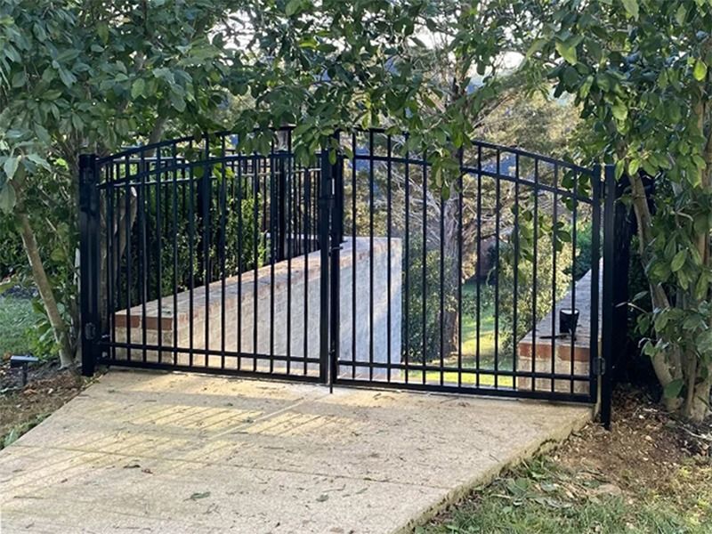 A black gate is surrounded by trees and a concrete walkway.