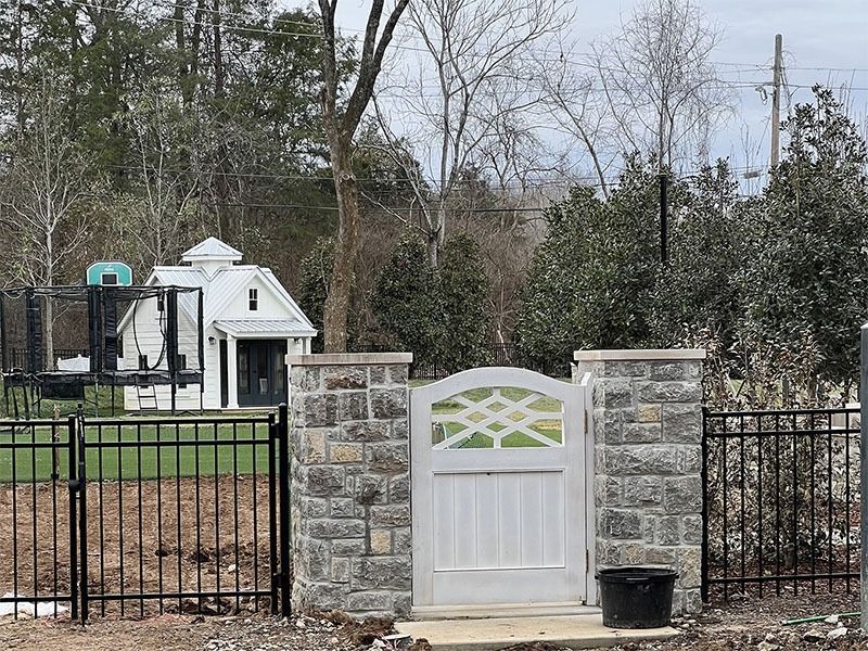 A white gate is surrounded by a stone wall and a metal fence.