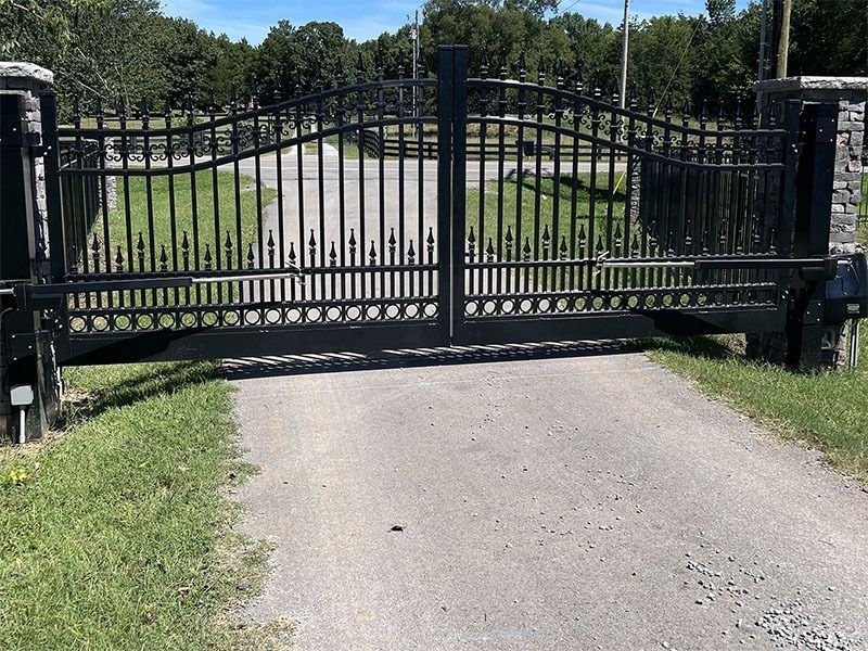 A black wrought iron gate is open to a dirt road.