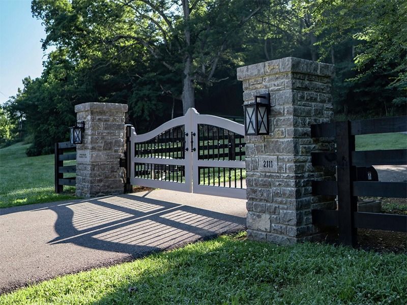 A white gate with a black railing is surrounded by stone pillars.