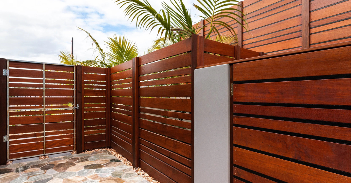 Wooden slat fence and gate surrounding an outdoor space, with a white wall section.