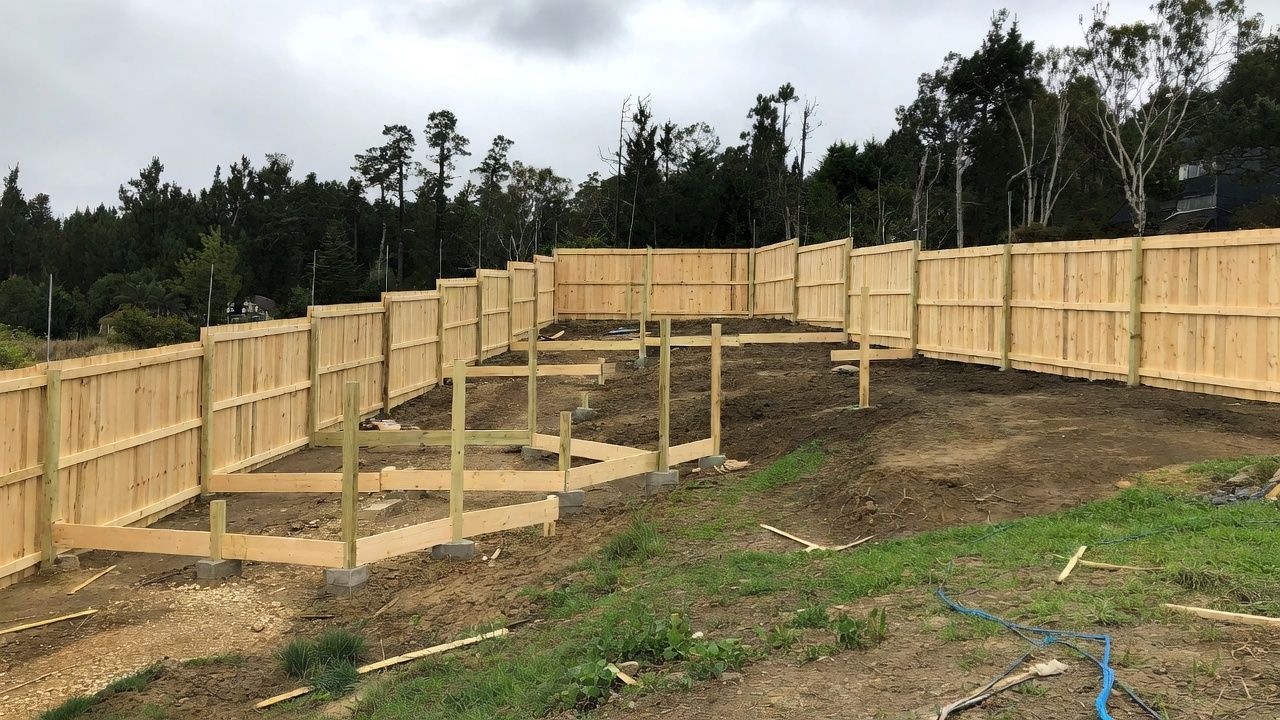 Wooden fence construction on a sloping hillside. Brown wood, green grass, and overcast sky.