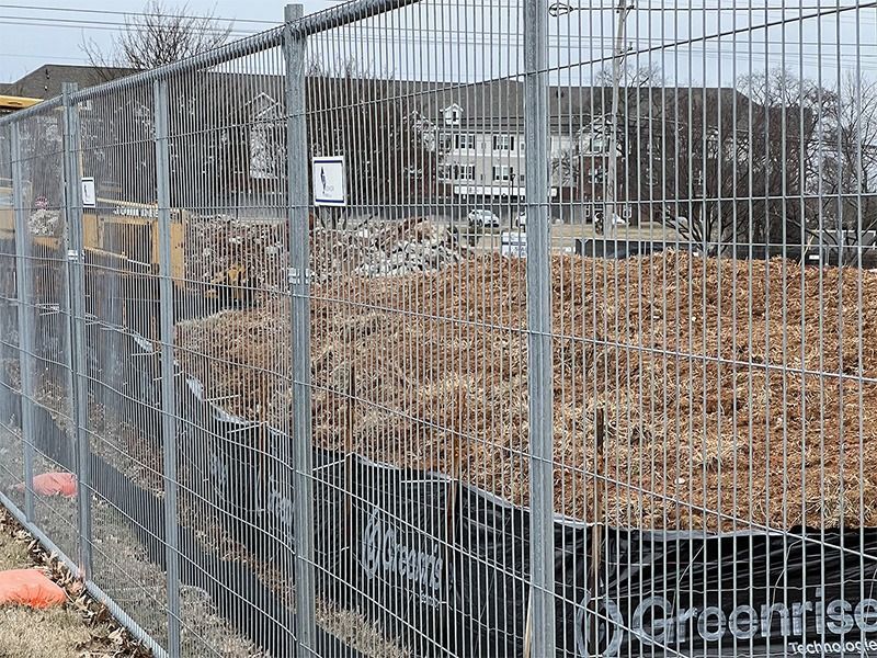 A fence surrounds a construction site with a lot of dirt behind it.