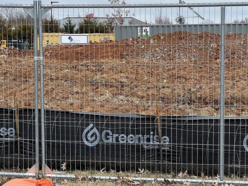 A large pile of dirt is behind a fence that says greenrise on it.