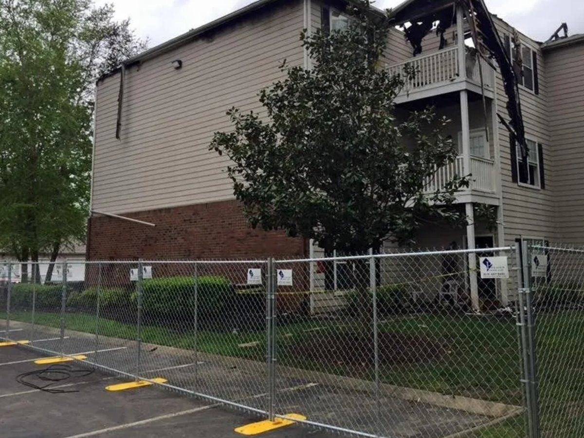 A chain link fence surrounds a parking lot in front of a building.