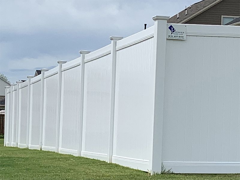 A white vinyl fence is sitting in the grass in front of a house.