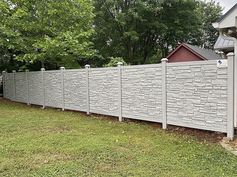 A stone fence surrounds a lush green yard in front of a house.