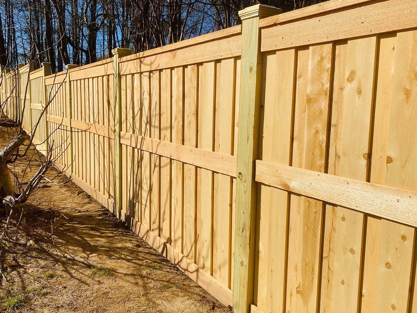 Wooden fence in a yard, vertical panels, light brown wood, tall posts.