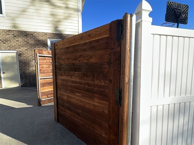 A wooden fence is next to a white fence in front of a house.