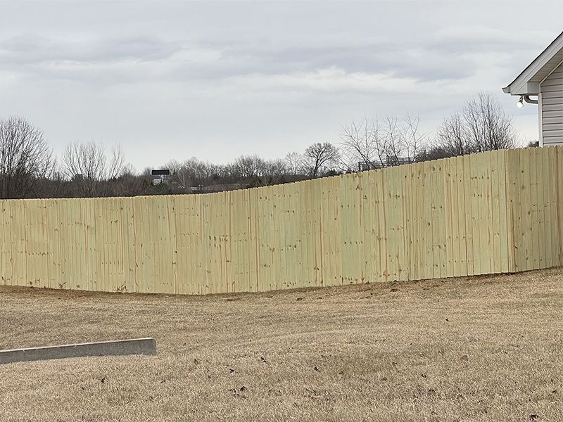 A wooden fence surrounds a grassy field in front of a house.