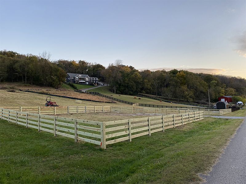 A wooden fence surrounds a field with a barn in the background.