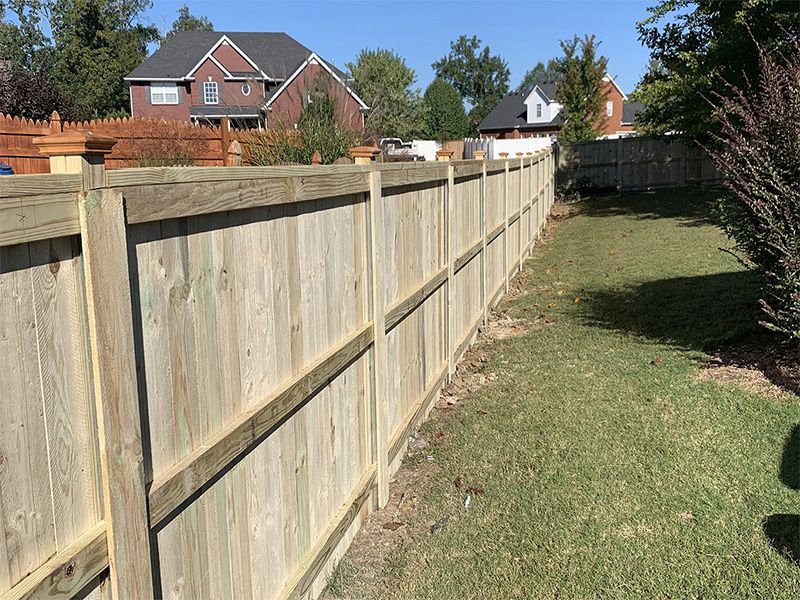 A wooden fence in a backyard with a house in the background.