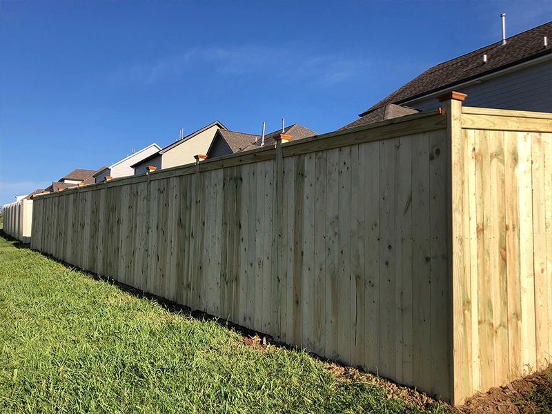 A wooden fence surrounds a lush green field in front of a house.