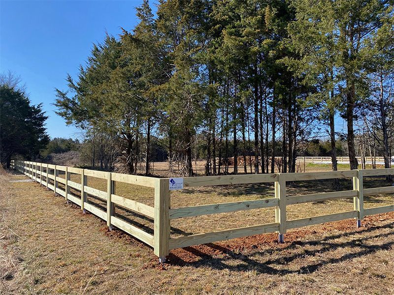 A wooden fence surrounds a field with trees in the background.