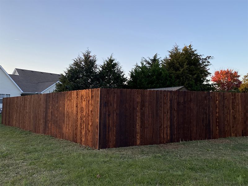 A wooden fence is surrounded by grass and trees in front of a house.