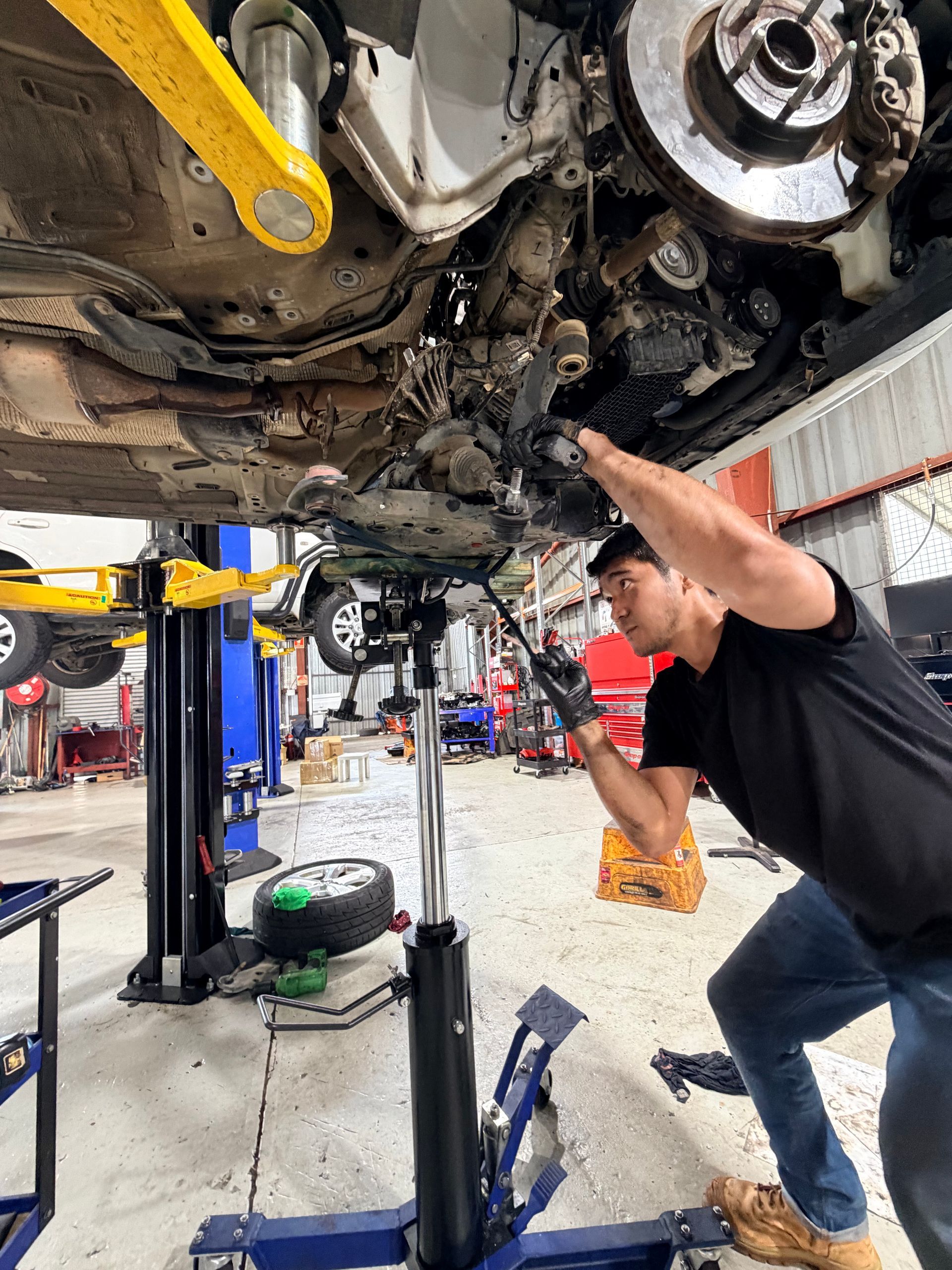 Mechanic working under a car lifted on a hoist in a repair shop.