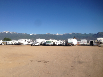 A row of rvs parked in a dirt lot with mountains in the background