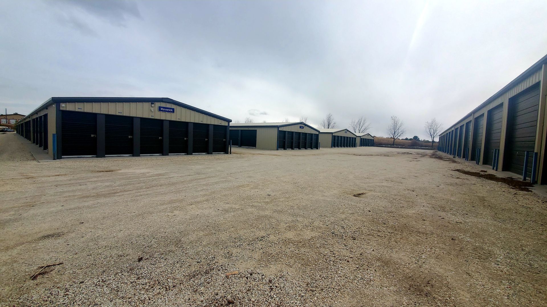 A row of storage units are lined up in a gravel lot.