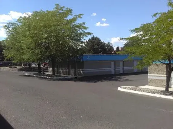 A building with a blue roof is surrounded by trees in a parking lot.