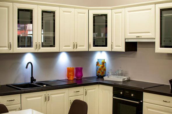 White kitchen cabinets with black countertops and sink. Glass-front cabinets, under-cabinet lighting, and orange and purple vases.