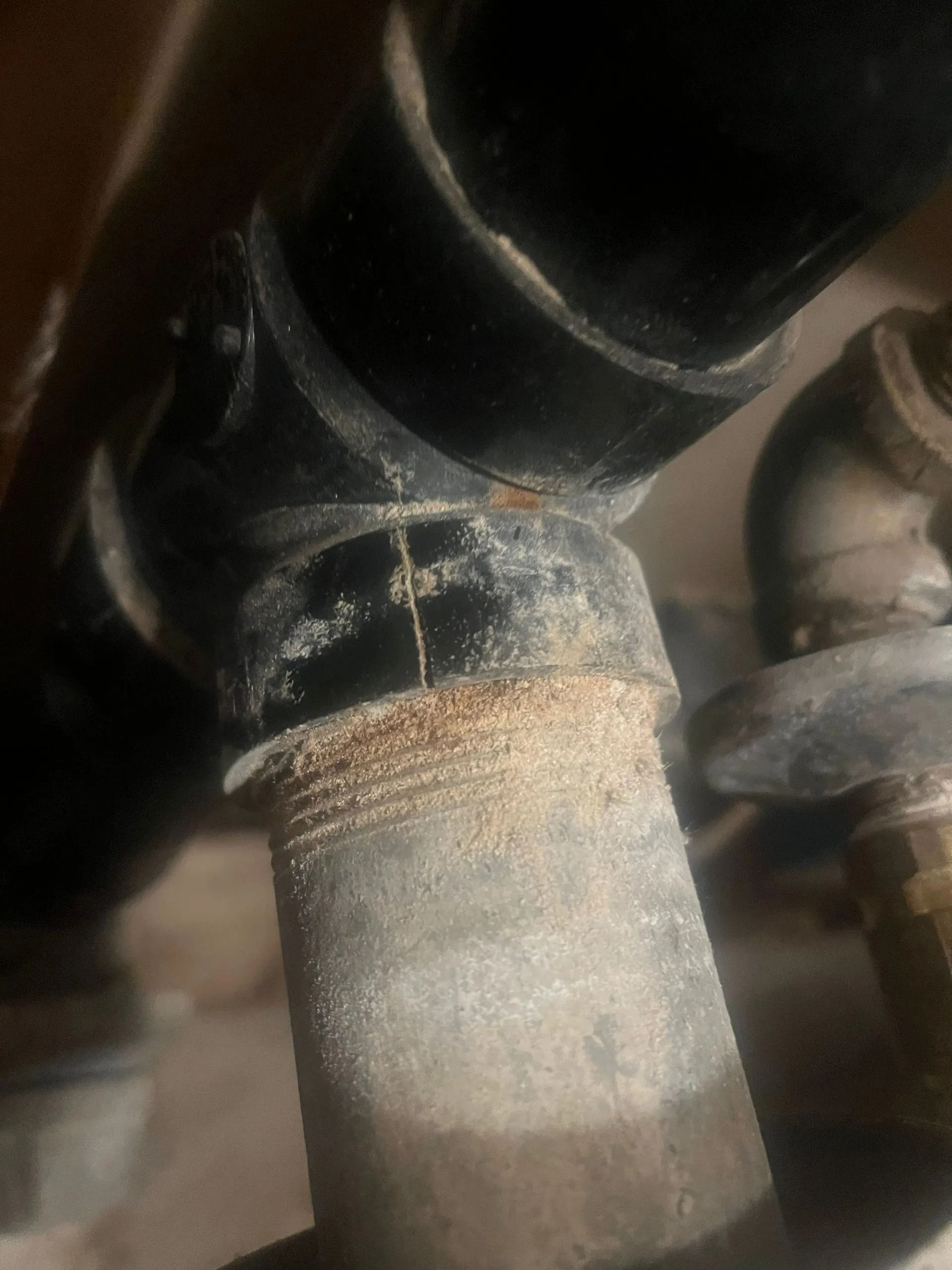 Close-up of plumbing pipes joined together, showing a crack and white residue.