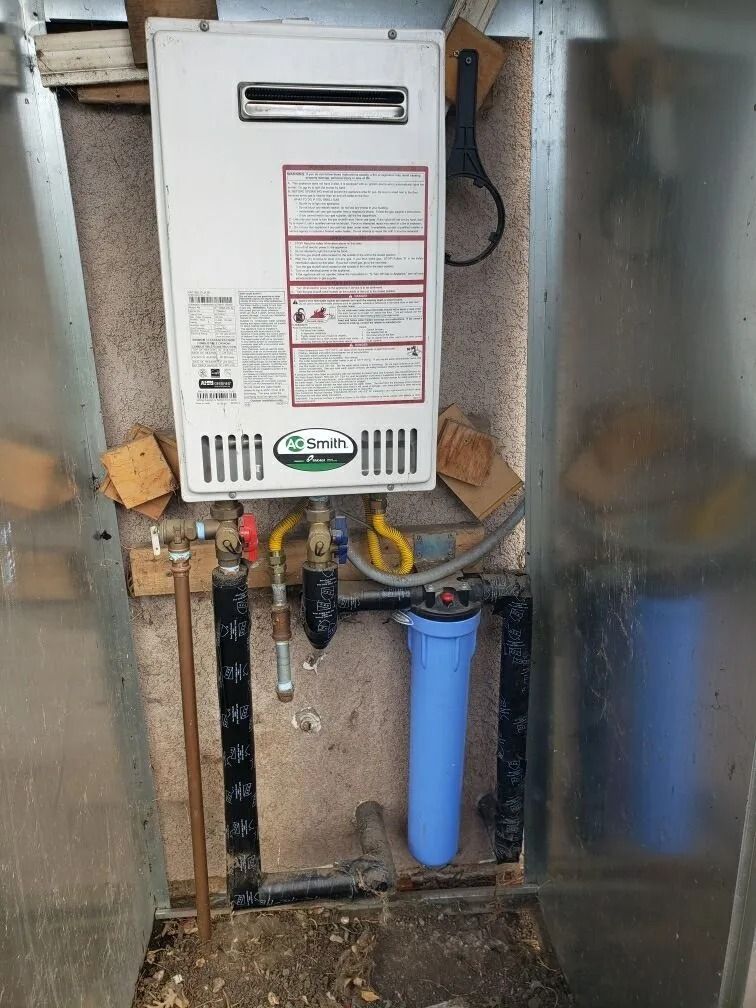 Tankless water heater and water filter installed on a metal wall inside a small enclosure.