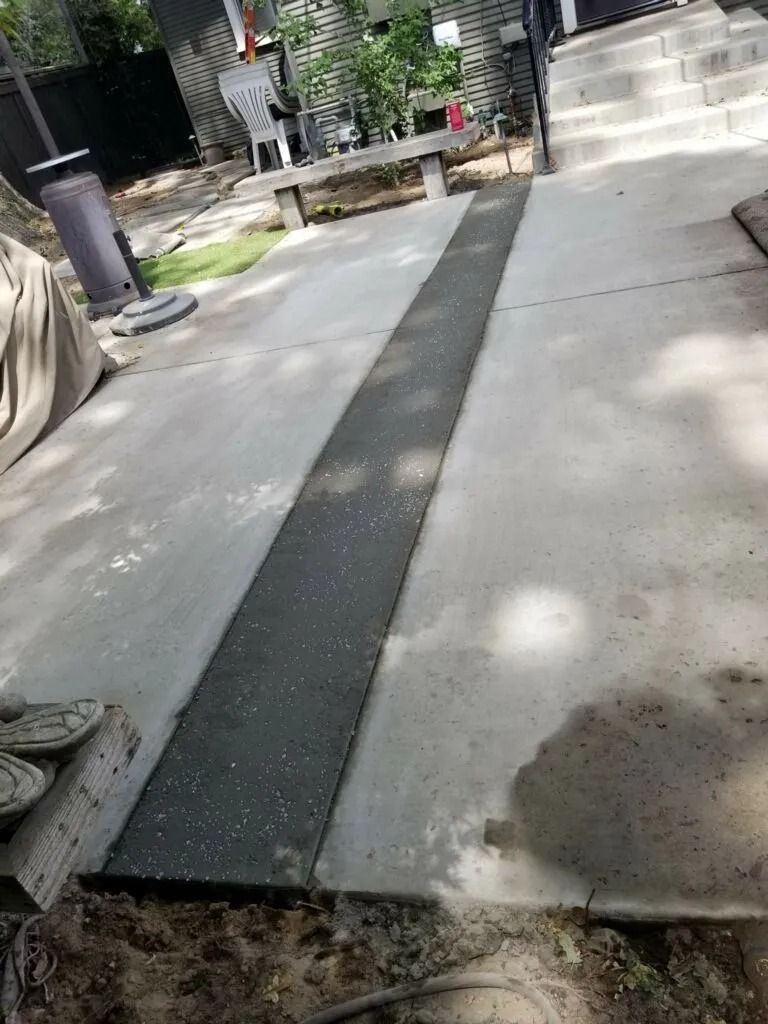 A narrow, textured concrete path is newly installed between two wider concrete slabs in an outdoor space.