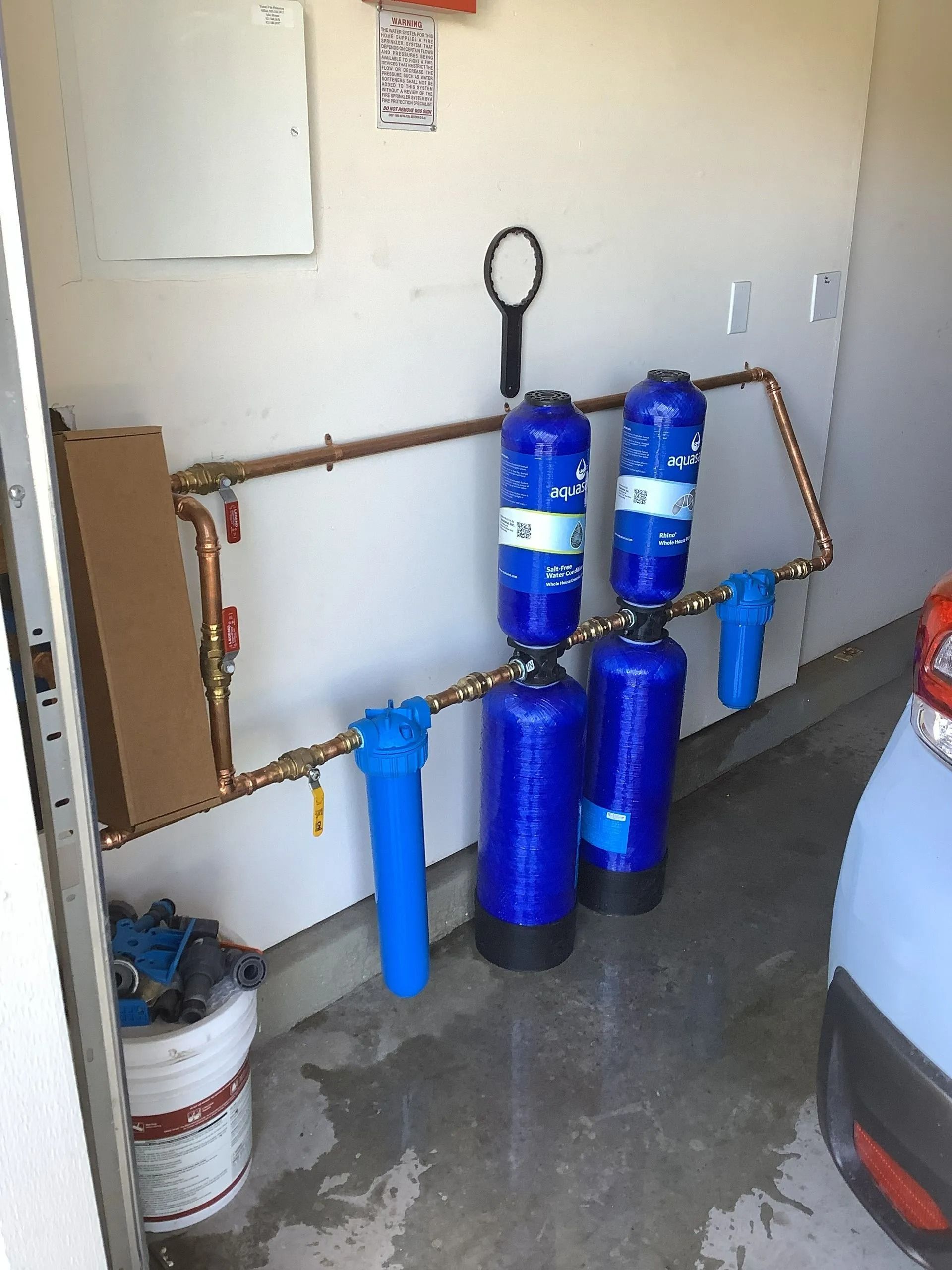 Water filtration system with blue tanks and copper pipes in a garage setting.