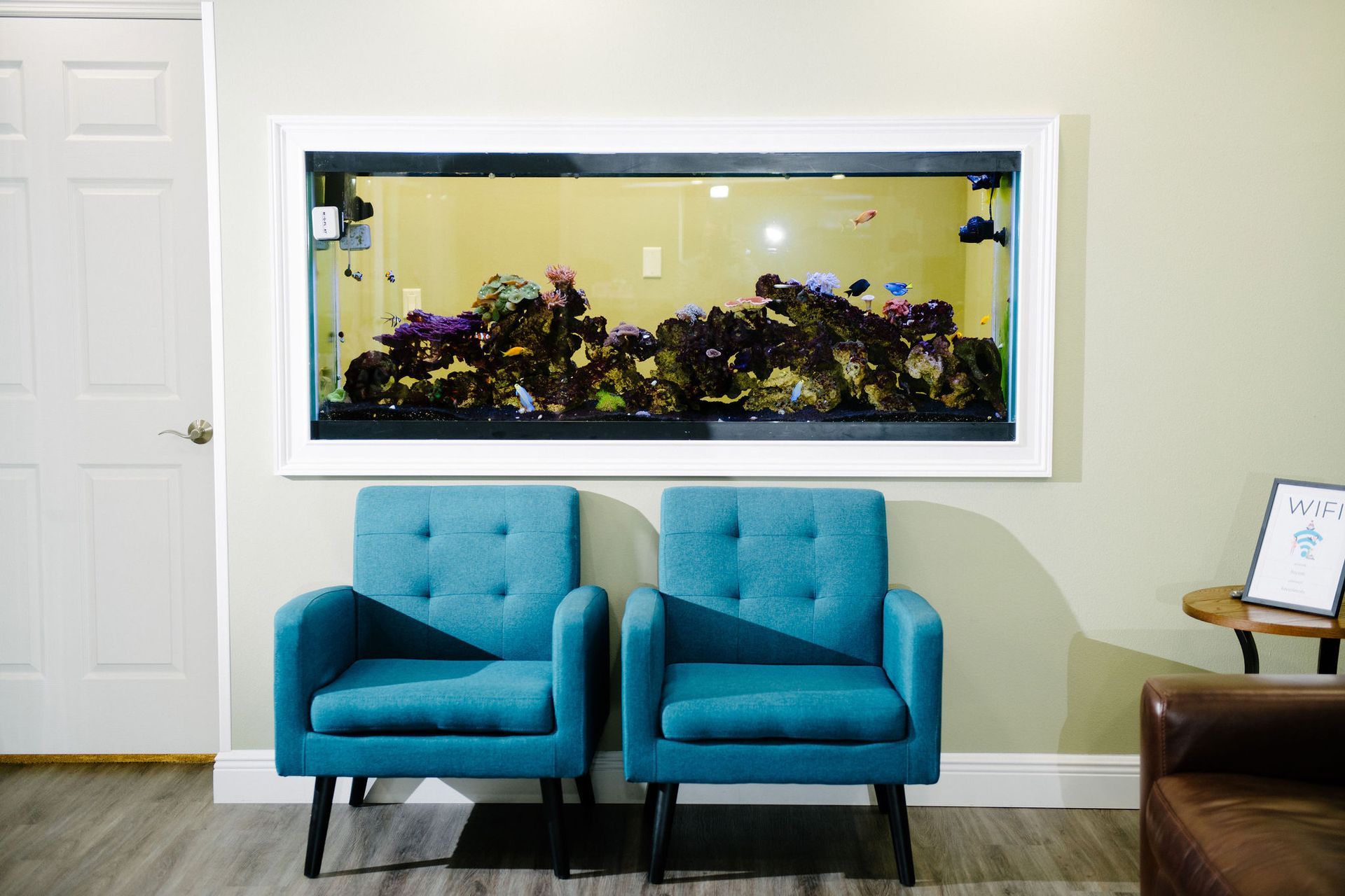 A waiting room with two blue chairs and an aquarium on the wall.