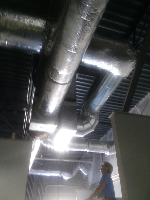 Man looking up at HVAC ductwork in a building. Shiny, silver ducts against a dark ceiling.