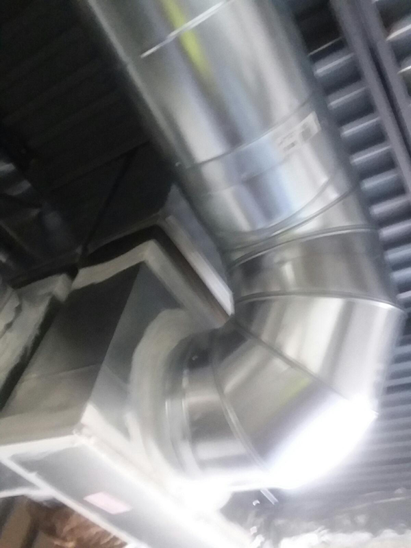 Metallic HVAC ductwork bends at a 90-degree angle, mounted on a ceiling with black insulation.