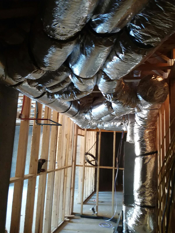 Flexible silver ductwork installed in the ceiling of a room under construction.