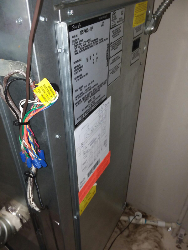 Furnace unit with wiring and labels attached in a utility room.