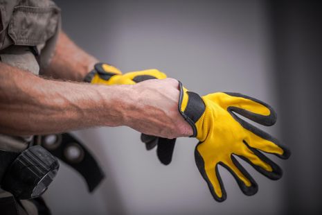 Person putting on bright yellow work gloves with black palms in a close-up shot