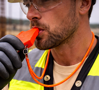Construction worker blowing a bright orange whistle, wearing a safety vest and gloves.