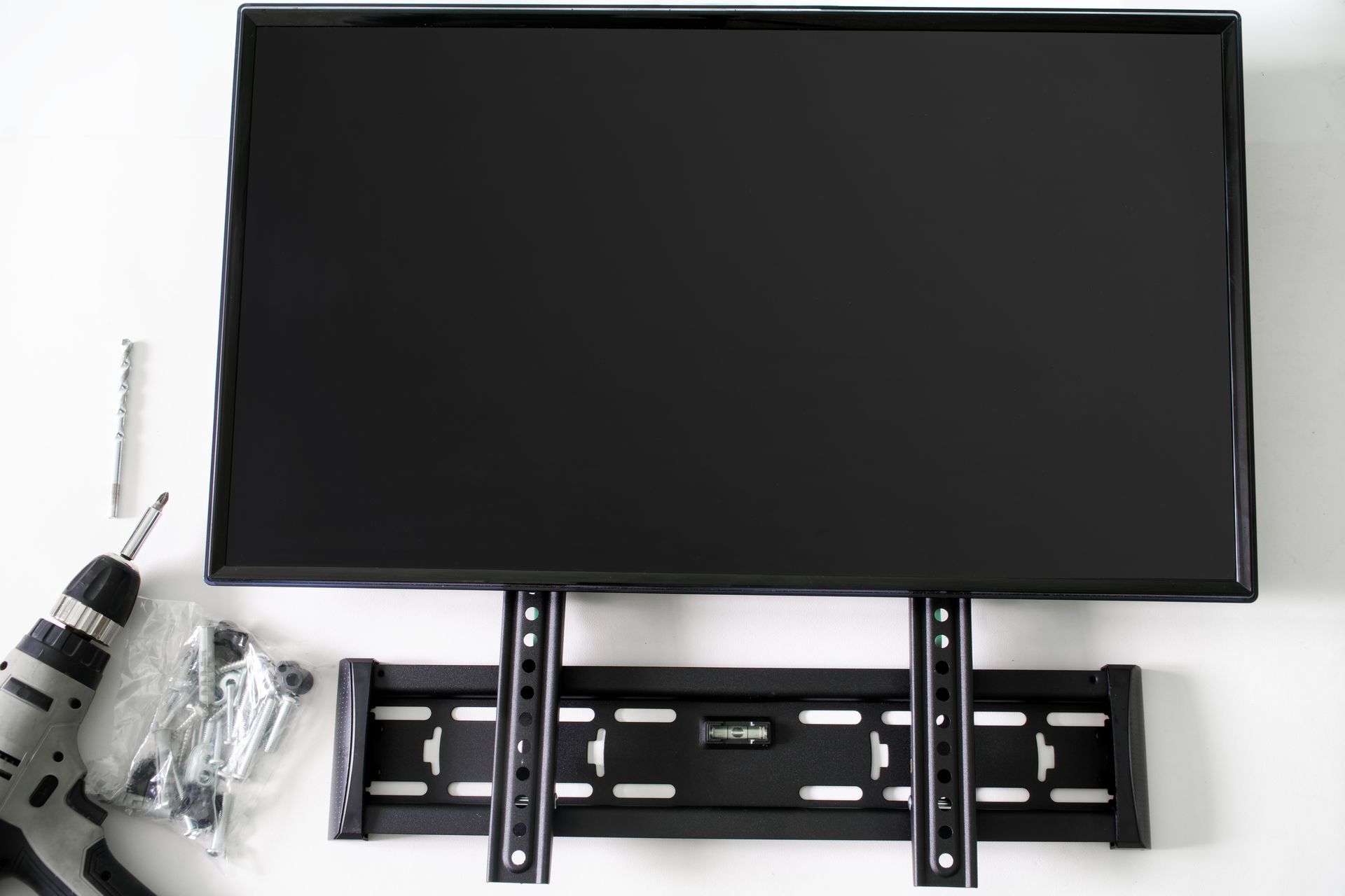 A flat screen tv is being mounted on a wall with a drill and screws.