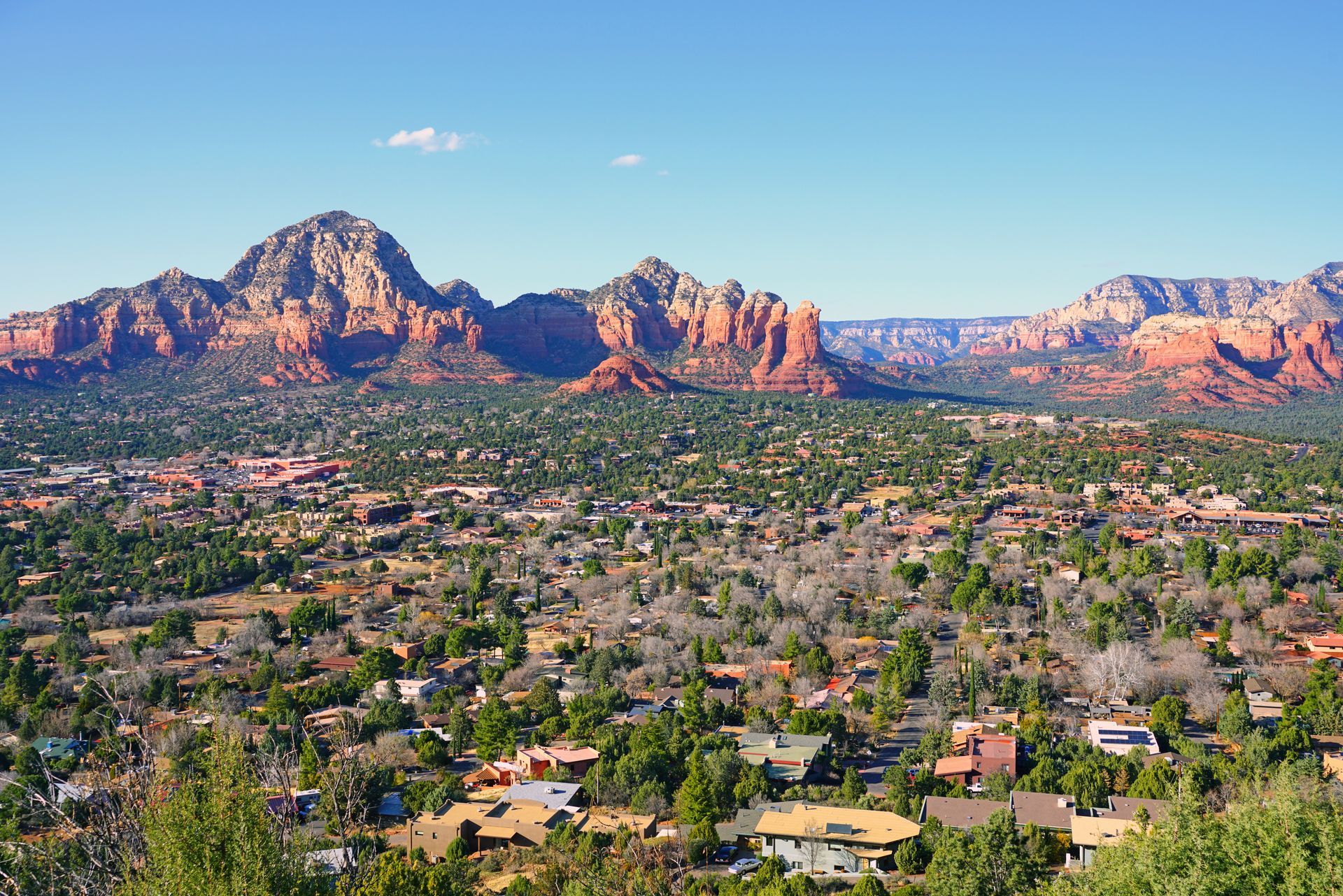 Red rock mountains overlooking a town of houses and trees under a blue sky.