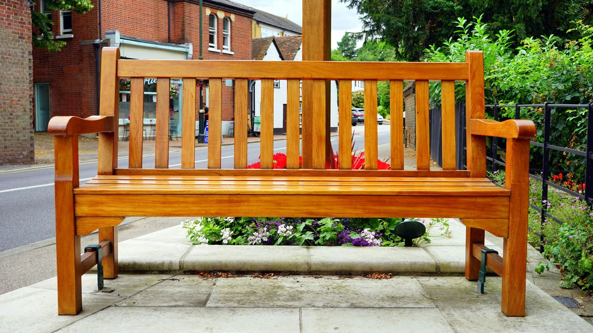 Wooden park bench with vertical back slats and armrests sits on a stone base, flowers in front.