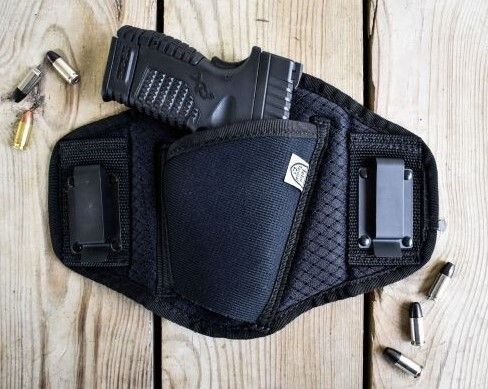 Black belly band holster with a handgun and magazine clip on a wooden surface.