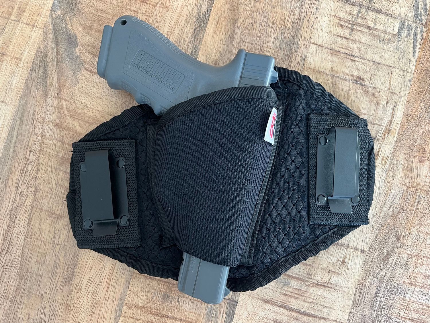 Black IWB holster holding a gray handgun, two black clips, on wood surface.