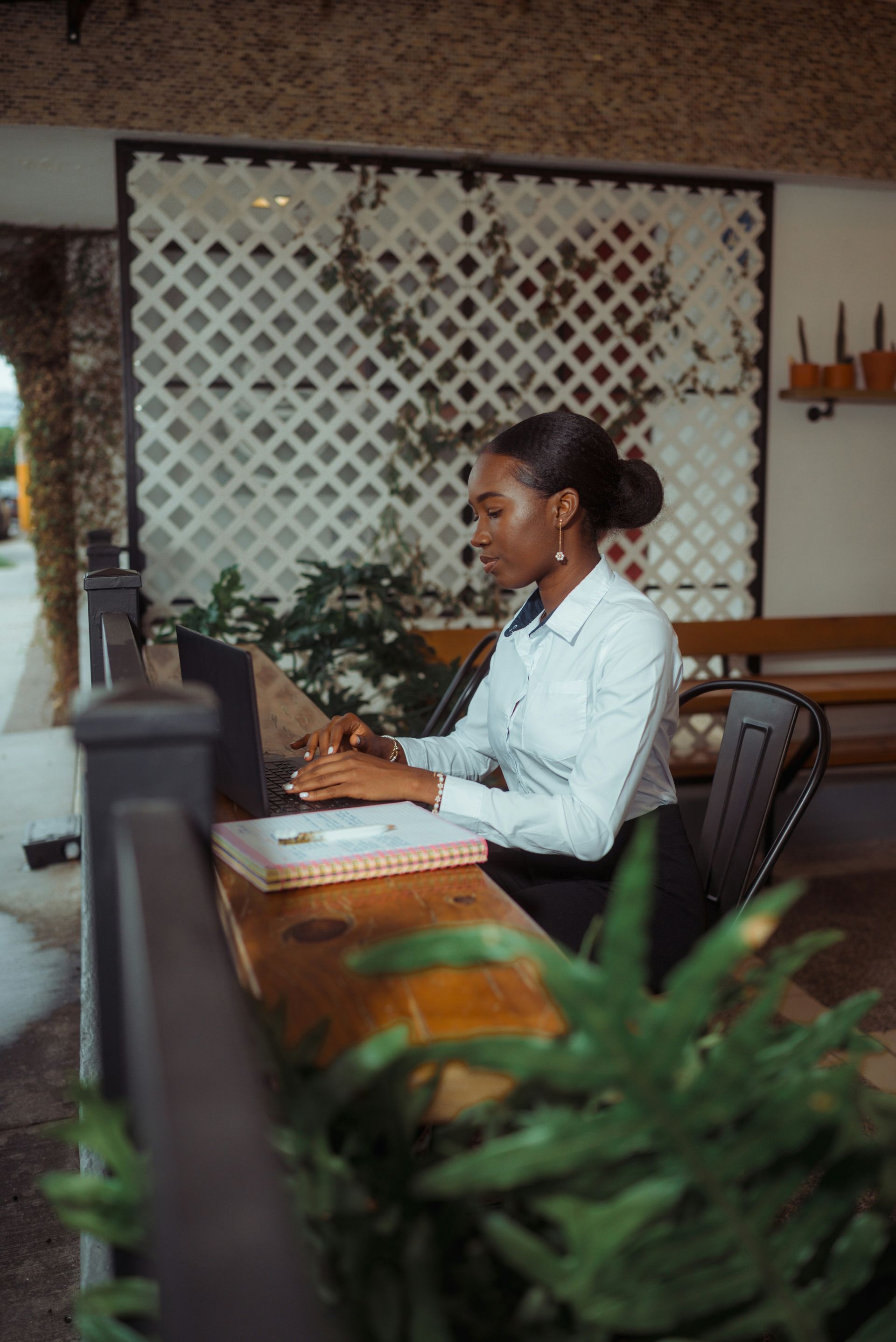 A person in a white button-down shirt works on a laptop at a wooden table in a brightly lit cafe with lattice decor.