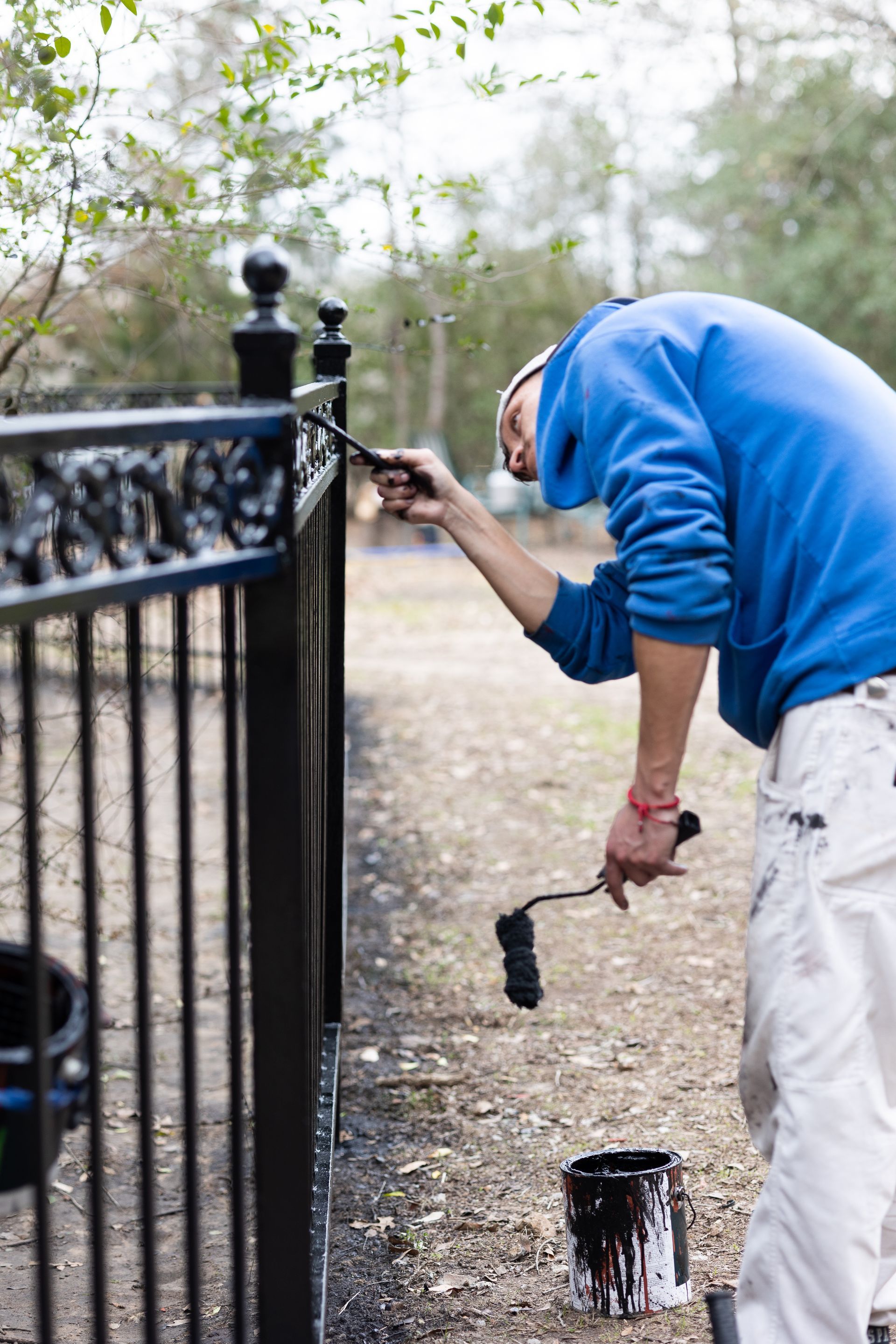 A man is painting a metal fence with a roller.