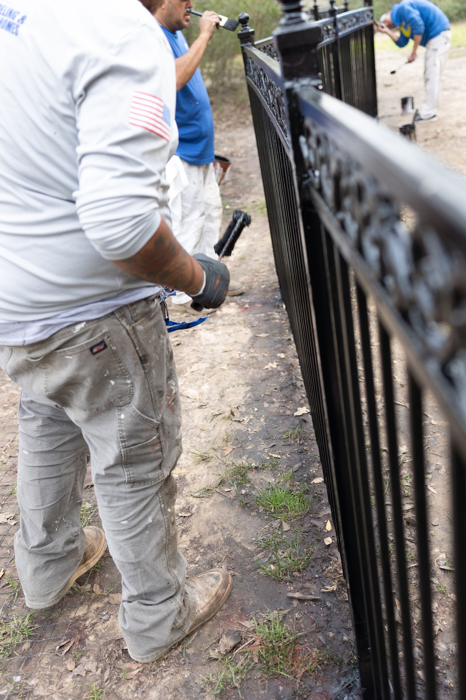 A man is painting a metal fence with a brush.
